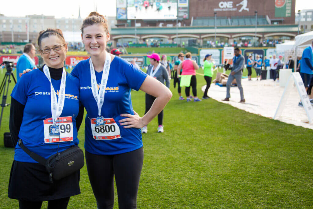 women runners pose and smile wearing running bib numbers and destiny rescue shirts