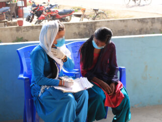 A border agent dressed in a sky-blue uniform interviews a girl at the Nepal border